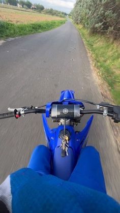 a person on a motor bike riding down a road with grass and trees in the background