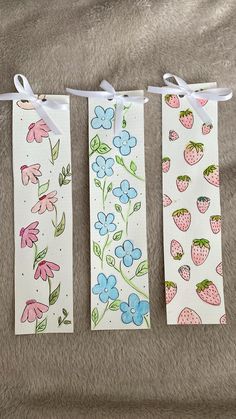 three bookmarks with flowers and strawberries on them are hanging from a line in front of a bed