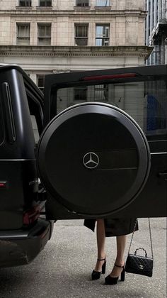 a woman is standing in front of a mercedes suv with the door open and her hand on the wheel