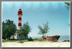 an old boat sitting on top of a beach next to a light house with a red and white striped roof