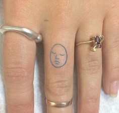 a woman's hand with two rings on it and a small face tattooed on the ring finger