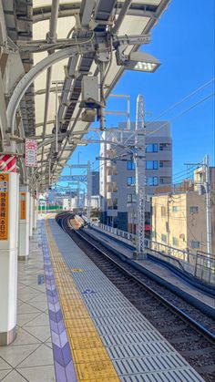 an empty train station with no people on the platform and buildings in the back ground