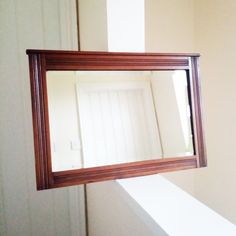 a mirror hanging on the side of a wall above a window in a room with white walls