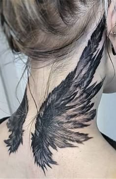 the back of a woman's neck is covered with black feathers and has a tattoo design on it