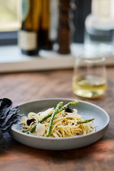 a white plate topped with pasta and asparagus next to a glass of wine