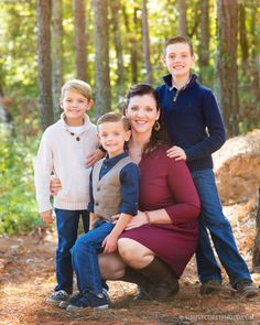 a woman and two boys are posing for a family photo in the woods with trees