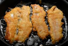 three pieces of fried fish cooking in a skillet