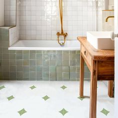 a bathroom with green and white tiles on the floor, sink and bathtub in it