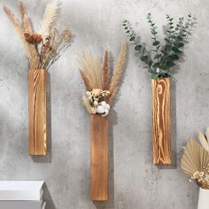 three wooden vases with dried flowers and plants in them on a gray wall background