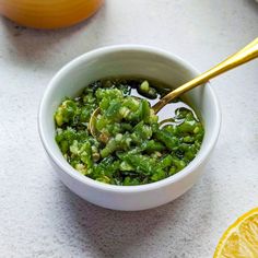 a white bowl filled with green vegetables next to sliced lemons and a spoon in it