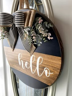 a wooden sign with the word hello painted on it and a bow hanging from it's front door