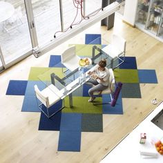 a woman is sitting at a table in the middle of a room with blue and green rugs