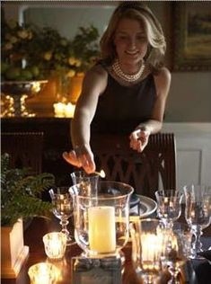 a woman standing in front of a table filled with glasses and candles on top of it