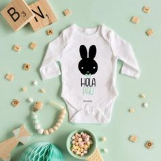 a baby's bodysuit with the words hola paa on it next to a bowl of candy