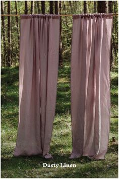 two pink curtains hanging from the side of a pole in front of trees and grass