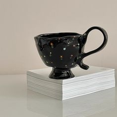 a black coffee cup sitting on top of a stack of paper with lights in it