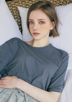 a woman laying on top of a bed next to pillows and pillow cases with her arms crossed