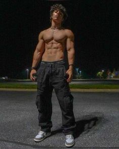 a shirtless man standing in the middle of a parking lot with his hands on his hips