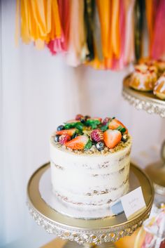 a white cake with fruit on top sitting on a gold platter next to other desserts