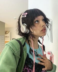 a woman wearing headphones and holding her hand up to her face while standing in front of a wall