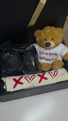 a brown teddy bear sitting in a black box with clothes and other items on it