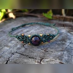 a green bracelet with a purple bead and gold beads on it sitting on a piece of wood