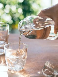 someone pouring water into a glass on top of a wooden table next to two empty glasses