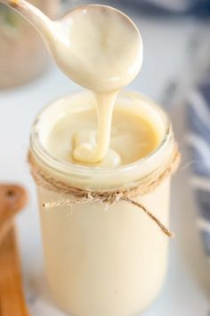 a spoon full of white liquid being poured into a glass jar with twine on it