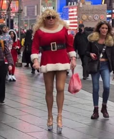 two women dressed as santa claus walk down the street in front of people on christmas day