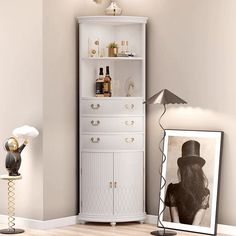 a tall white cabinet sitting next to a wall with pictures on it and a lamp