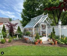 a small white greenhouse with potted plants in the front and on the back side