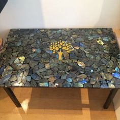 a table made out of rocks with a tree logo on the top and blue glass pebbles around it