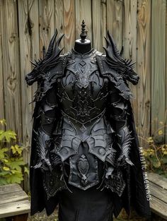 a costume made out of black leather with spikes on the shoulders and wings, is displayed in front of a wooden fence