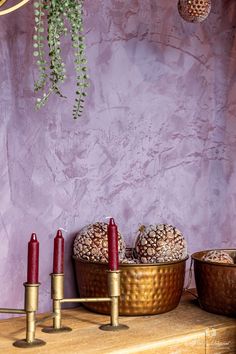 some candles are sitting on a table next to two bowls with pine cones in them