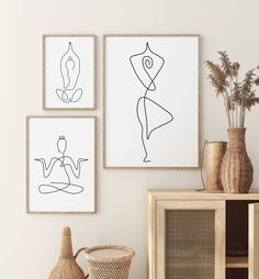 three framed art pieces hang on the wall above a wicker basket and vases