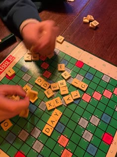 two hands playing scrabble on a board game with letters and numbers scattered around it