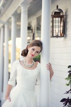 a woman in a white dress leaning against a pillar