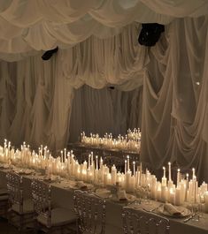 a long table with many candles on it and white drapes hanging from the ceiling