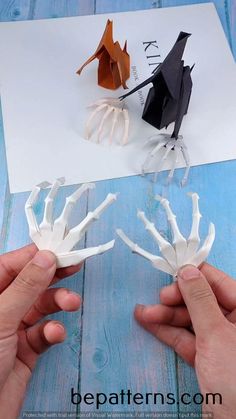 two hands are holding fake skeleton hands in front of an origami bird