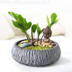 there is a small potted plant in the shape of a buddha statue with rocks and plants