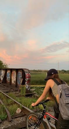 a woman with a backpack is riding her bike on the railroad tracks near an abandoned train track