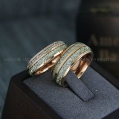 two gold wedding rings sitting on top of a black display case with the ring in it's center