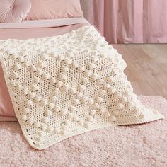 a white crocheted blanket sitting on top of a bed next to a pink pillow