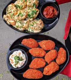 two black plates filled with food on top of a cement floor next to a red pillow