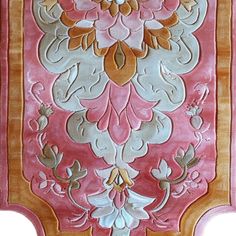 an ornate pink and gold wall hanging with flowers on it's side, in the middle