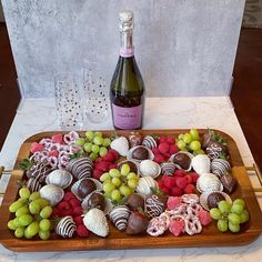 a wooden platter filled with chocolate covered strawberries and grapes next to a bottle of wine