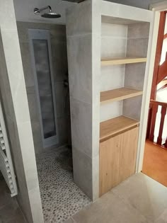 a walk in shower sitting next to a wooden shelf on top of a tiled floor