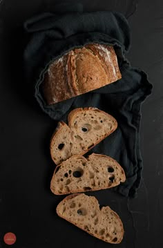 some bread is laying on top of a black cloth next to two pieces of bread