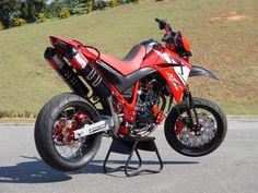 a red and black motorcycle parked on the side of a road next to a hill