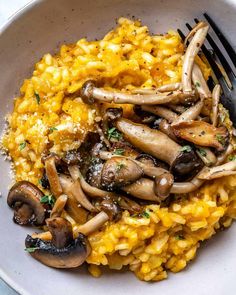 a white bowl filled with rice and mushrooms next to a fork on top of it